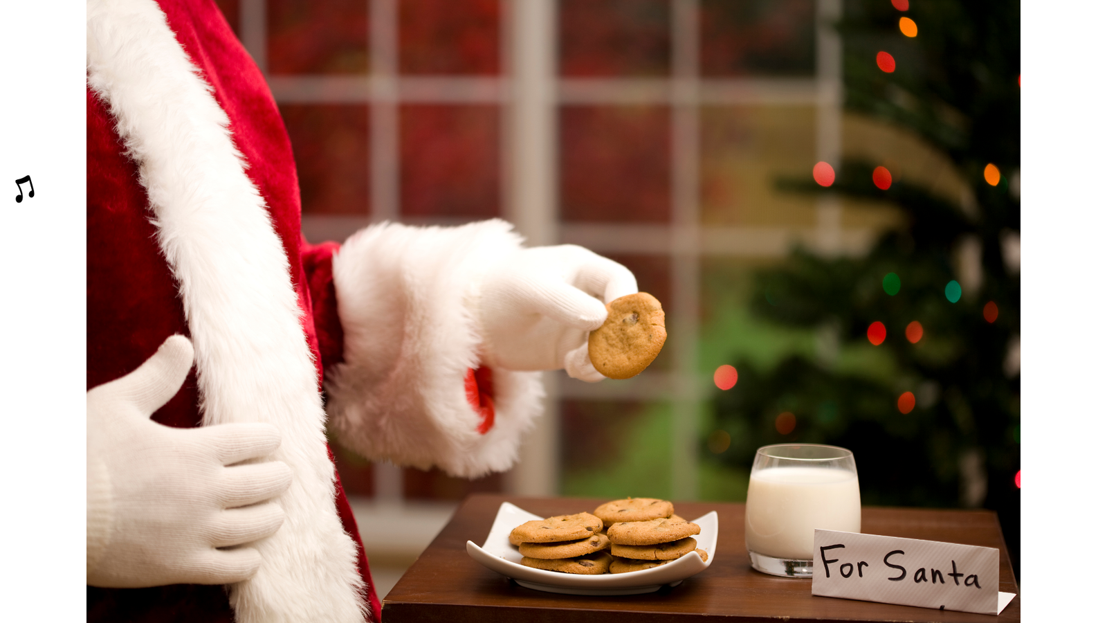 Santa Clause mit einem Keks in der Hand, Keksen, Milch und Schild auf dem Tisch