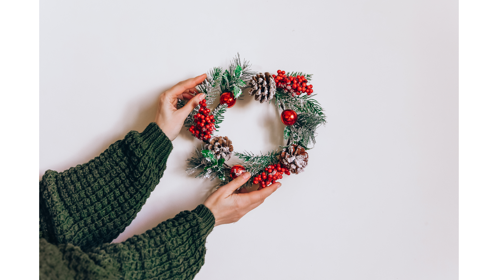 Adventskranz, der von zwei Händen an eine Wand gehalten wird